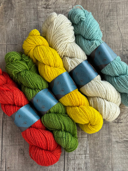 Five skeins of yarn in red, green, yellow, cream, and light blue, arranged diagonally on a gray wood background. Each skein is wrapped with a blue paper band.